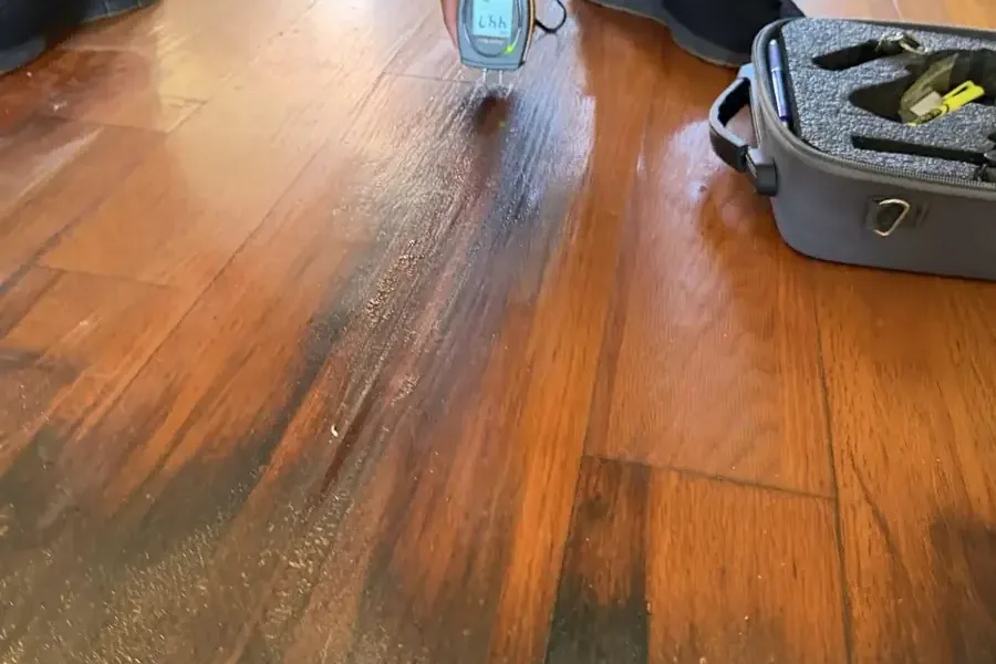 A moisture meter testing wet hardwood boards beside a tool case